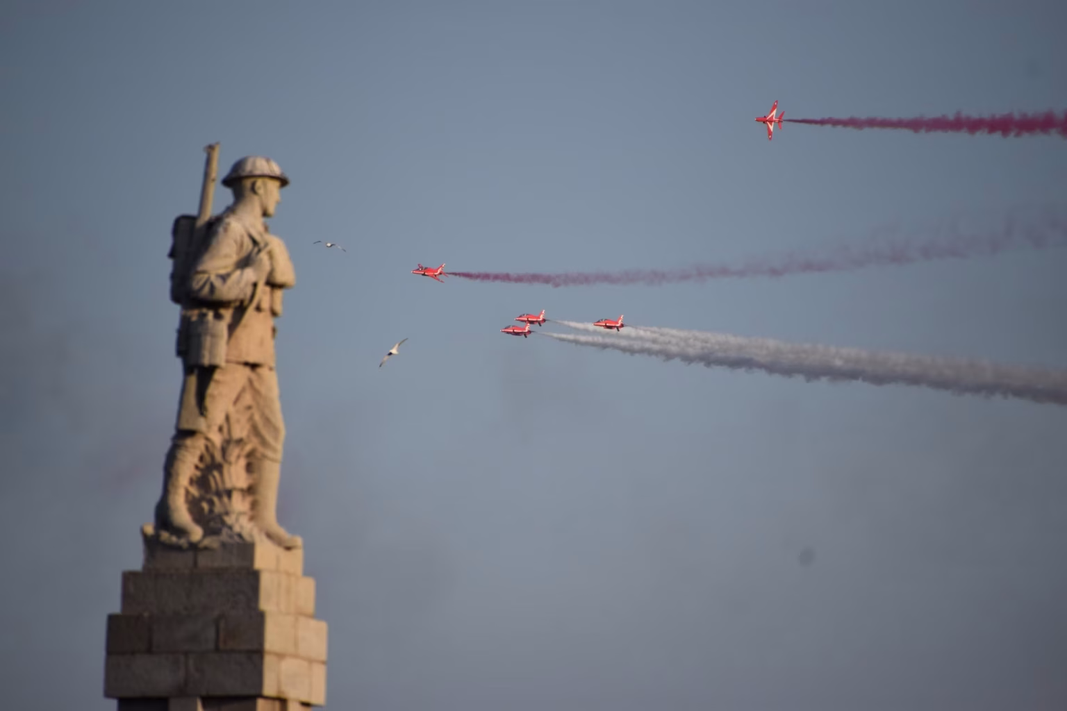The Red Arrows flying past a memorial statue